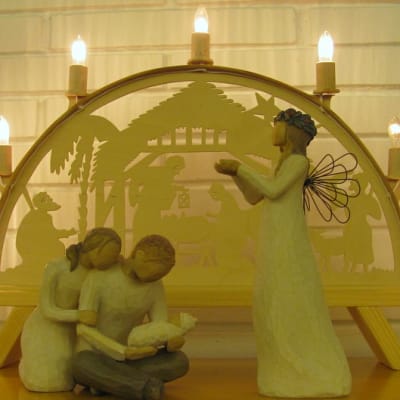 Puusta veistetyt Maria ja Joosef Jeesus-lapsen kanssa vierellään enkeli. Taustalla puinen kynttelikkö. 