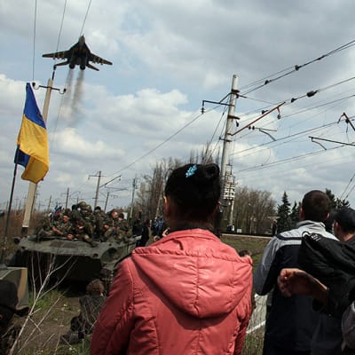 Ukrainalaisen panssarikolonnan pysäyttäneet venäläismieliset ihmiset katselevat ukrainalishävittäjän ylilentoa Kramatorskin kaupungin ulkopuolella.