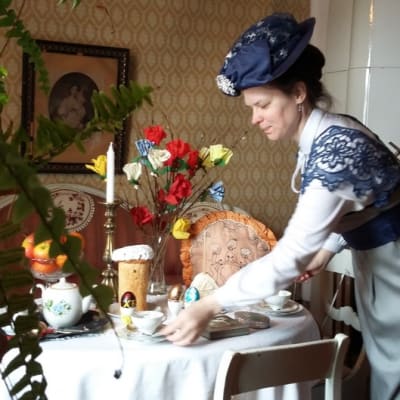 Historialliseen asuun pukeutunut nainen laittaa kahvipöytää