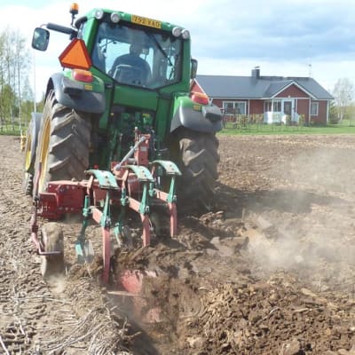 Maanviljelijä kyntämässä peltoa traktorilla.
