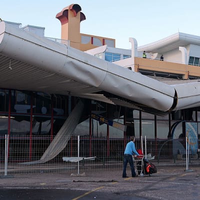 Matkustaja ohittaa myrskyssä vaurioituneen Faron lentokentän terminaalin.