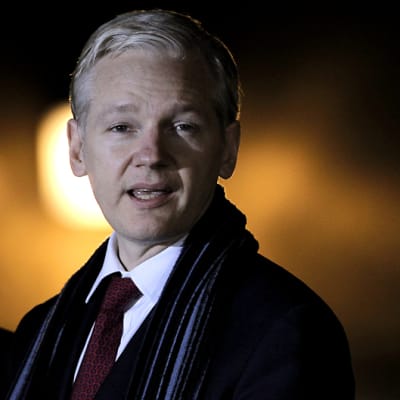Julian Assange kuvattuna yöllä dramaattinen takavalo takanaan.
