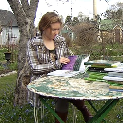 Nainen lukee kirjoja puutarhassa.