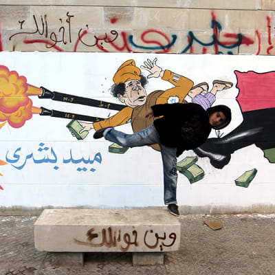 Poika potkaisee kohti Muammar Gaddafia esittävää seinämaalausta.