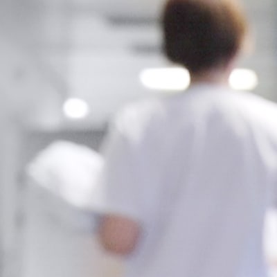En sjukvårdare med ryggen mot kameran i en sjukhuskorridor.