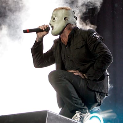 Laulajalla on harmaa maski päässään, takaa nousee savusumua.