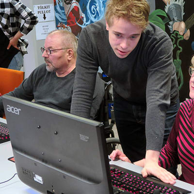 Nuori mies opastaa vanhempaa naista tietokoneen äärellä