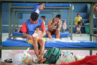 Pappor och barn sitter i våningssängar med blå lakan i en flyktingförläggning i Manaus i Brasilien.