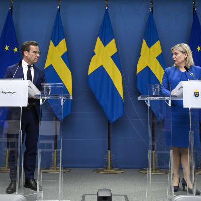 Moderatledaren Ulf Kristersson och Sveriges socialdemokratiska statsminister Magdalena Andersson framför varsitt podium med svenska och EU-flaggor i bakgrunden.