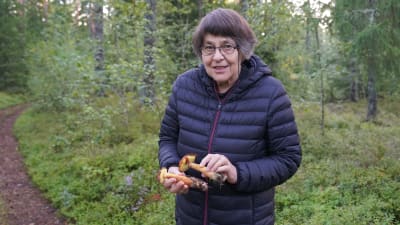 En kvinna står i skogen med svampar i sina händer.