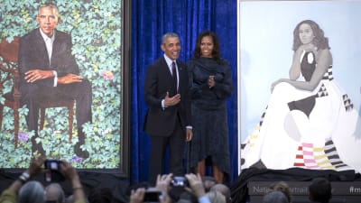 Storleende Barack och Michelle Obama på scen av sidan av de nymålade porträtten av dem i Washington DC.
