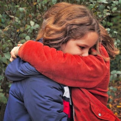 Kaksi nuorta tyttöä halaa toisiaan ulkona.