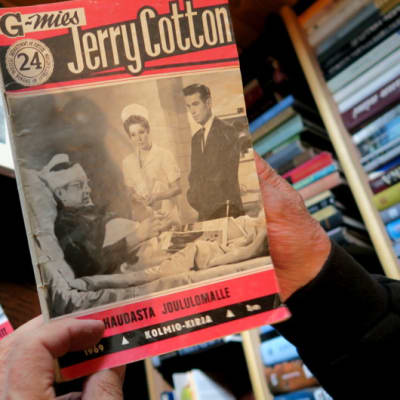 Jerry Cottonin numero 24 miehen käsissä, pöydällä lisää Cotton-lehtiä
