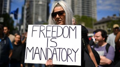 Demonstrant i Melbourne som håller upp en skylt där det står "Freedom is mandatory".