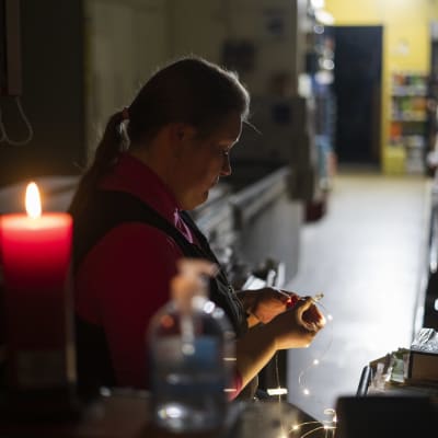 Mari Heikkinen laittaa kauppaan valoja sähkökatkon aikana kynttilän ja akkuvalon loisteessa.