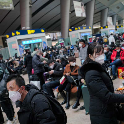 Matkustajat odottavat junaa kasvomaskit kasvoillaan Pekingin juna-asemalla uudenvuoden aattona.
