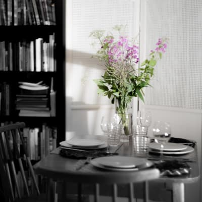 En bukett blommor på ett bord med en enkel festdukning. Endast blommorna har färg i bilden, allt annat är svartvitt.