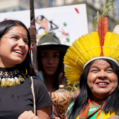 två kvinnor från ursprungsbefolkningen i ecuador, en äldre och en yngre, står bredvid varandra i en demonstration. de har färgglatt halsband och huvudbonad på sig och den yngre kvinnan är målad i ansiktet