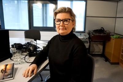 Kvinna i svart polotröja och glasögon sitter i en radiostudio.
