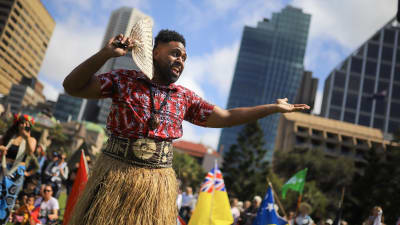 Man klädd i traditionell dräkt gestikulerar under klimatstrejk i Sydney.