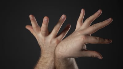 Närbild på två händer som sprätar ut med fingrarna med en mörk bakgrund. 