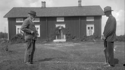 Två män leker "dra girsnot", där man ska försöka få omkull sin motståndare genom att dra i ett rep som är fastspänt mellan de tävlandes vrister. Bilden är tagen 1930 i Finström, Åland.