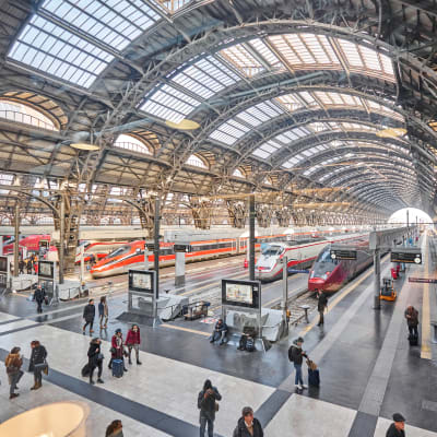 Bild inifrån Milanos centralstation, med flera vitröda strömlinjeformade tåg på olika spår bredvid varandra.