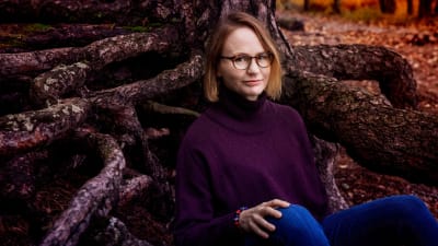 Författaren Maria Grundvall sitter i skogen.