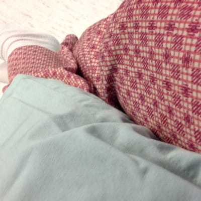 Potilas istuu sairaalasängyllä leikkausvaatteet päällään.