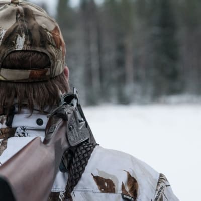 Metsästäjä takaapäin kuvattuna ase olalla.