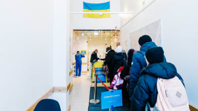 Flyktingar som köar. På väggen ovanför dem hänger en ukrainsk flagga.