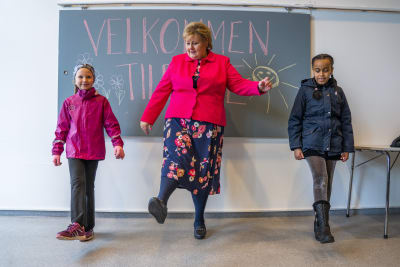 Erna Solberg övar distanshälsningar med två skolelever.