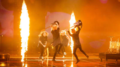 Blind Channel uppträder på eurovisionsscenen. De hoppar i en ring med elgitarrerna höjda och eldpelare runt dem.