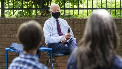 Joe Biden sitter på en stol och blir intervjuad. Han bär ansiktsskydd.
