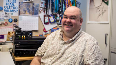 Johan Lindroos sitter med en ljus kragskjorta på sig i ett arbetsrum. Han ser glad ut och ser in i kameran.