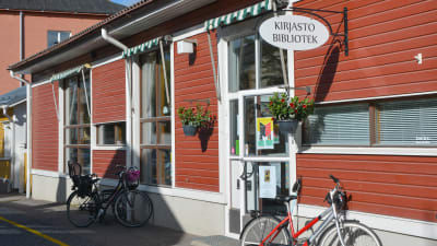rött trähus med skylten bibliotek utanför, cykel parkerad framför dörren