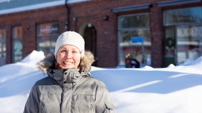 En kvinna står ute i soligt vinterväder och ler in i kameran.