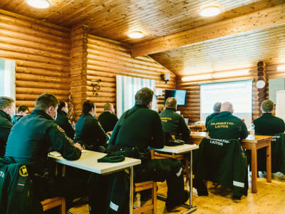 Gränsbevakningsarbetare sitter vid bord i en stockstuga och lär sig om att använda hundar i arbetet.