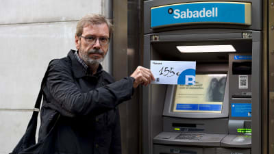 Joaquim Curbet deltog i protesten på fredag och visar upp ett kuvert med de 155 euro som han lyfte från Banc Sabadell i Barcelona. Han sade sig hoppas att protesten "ökar trycket mot den spanska regeringen".