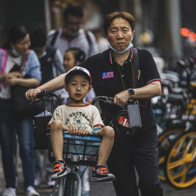 En pappa som leder sin cykel med sitt barn som sitter i cykelkorgen. 