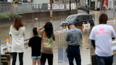 En grupp människor står och tittar på en översvämmad väg i Higohiroshima. 