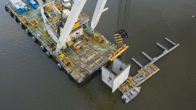 Stora betongelement sätts på plats i hamnbassängen i Vasa hamn med hjälp av en specialkran som står på en ponton.