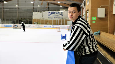 Isak Gull är ishockeydomare för yngre lag. Han står i domarskjorta utanför isen i Närpes ishall.