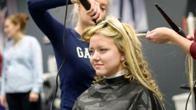 En blond kvinna får sitt hår lockat av två frisörstuderande.