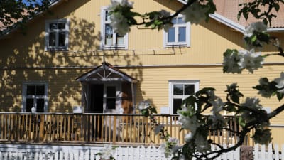 Ett gult stort hus (gästgiveri). I förgrunden grenar från ett blommande äppelträd.