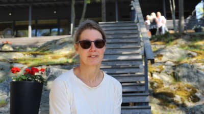 En kvinna i solglasögon sitter på en trappa vid en stuga utomhus. 