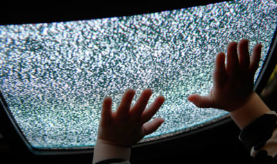 En barn rör en tv med brus på skärmen.
