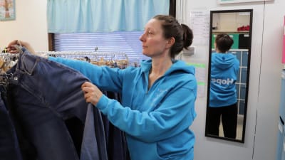 Maria Vesa sorterar jeans som hänger på hängare.