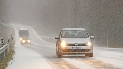 Bil kör fram längs väg i snöyra.