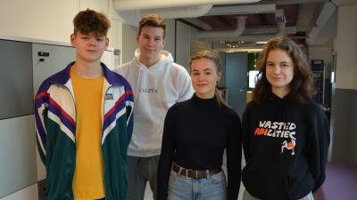 Fyra ungdomar står på rad i en skolkorridor.